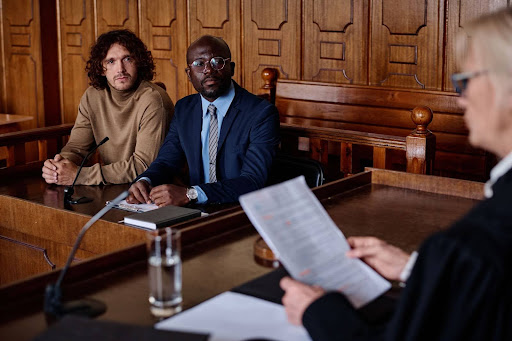 A judge looking at a document while in court as two men sit, looking at her in silence.