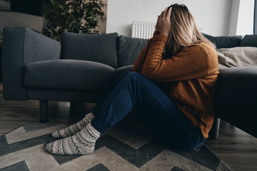 A distressed woman sits on her living room floor