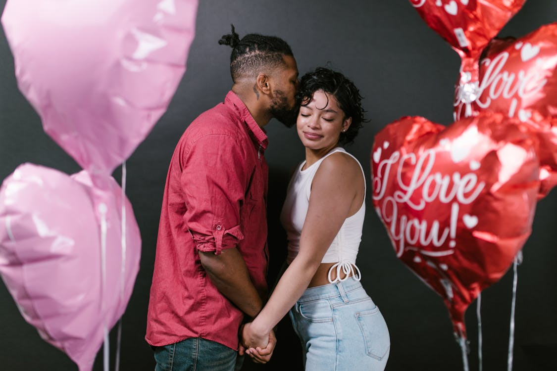 Couple holding hands beside heart-shaped Valentine’s balloons.