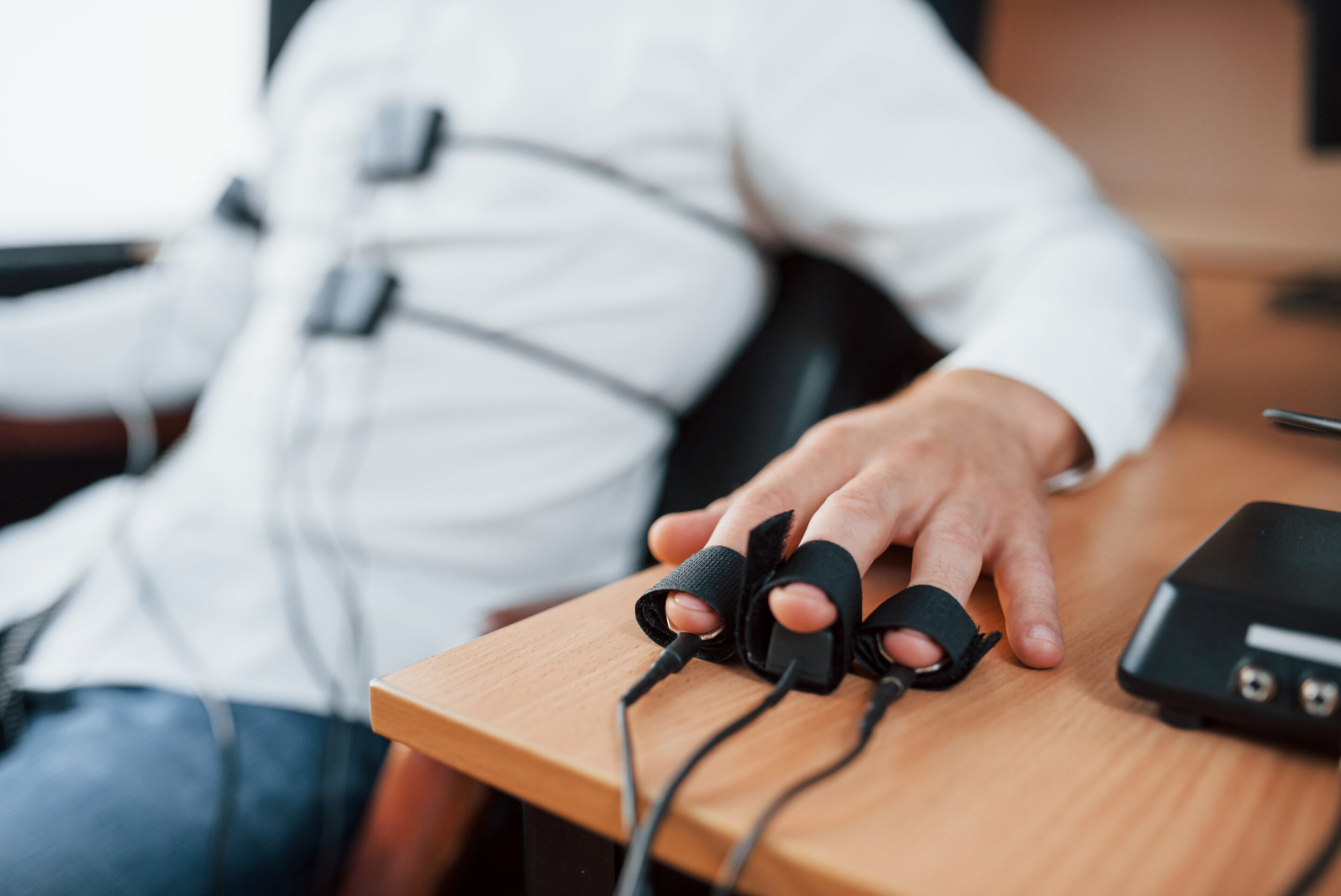 man connected to a polygraph machine with finger electrodes during a lie detector test in an office