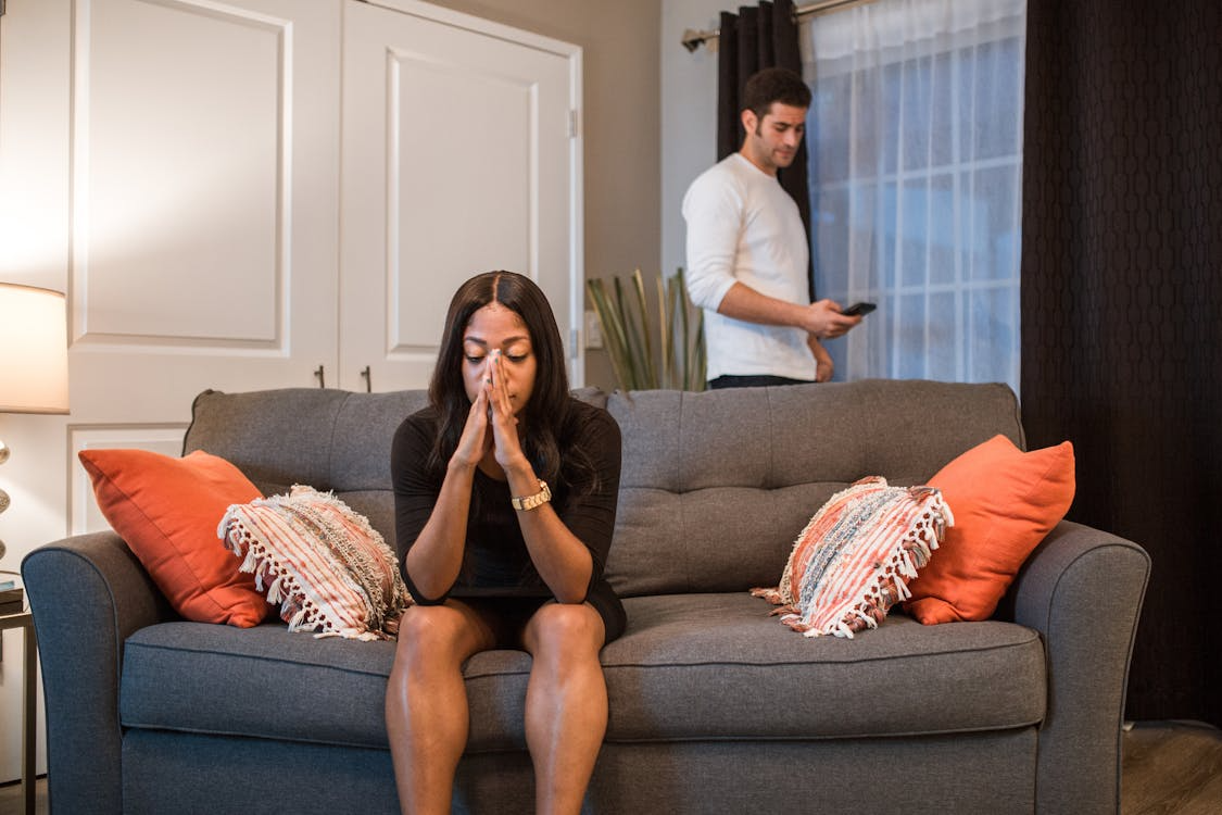 A woman sitting on a sofa while a man is standing at the back looking at his phone