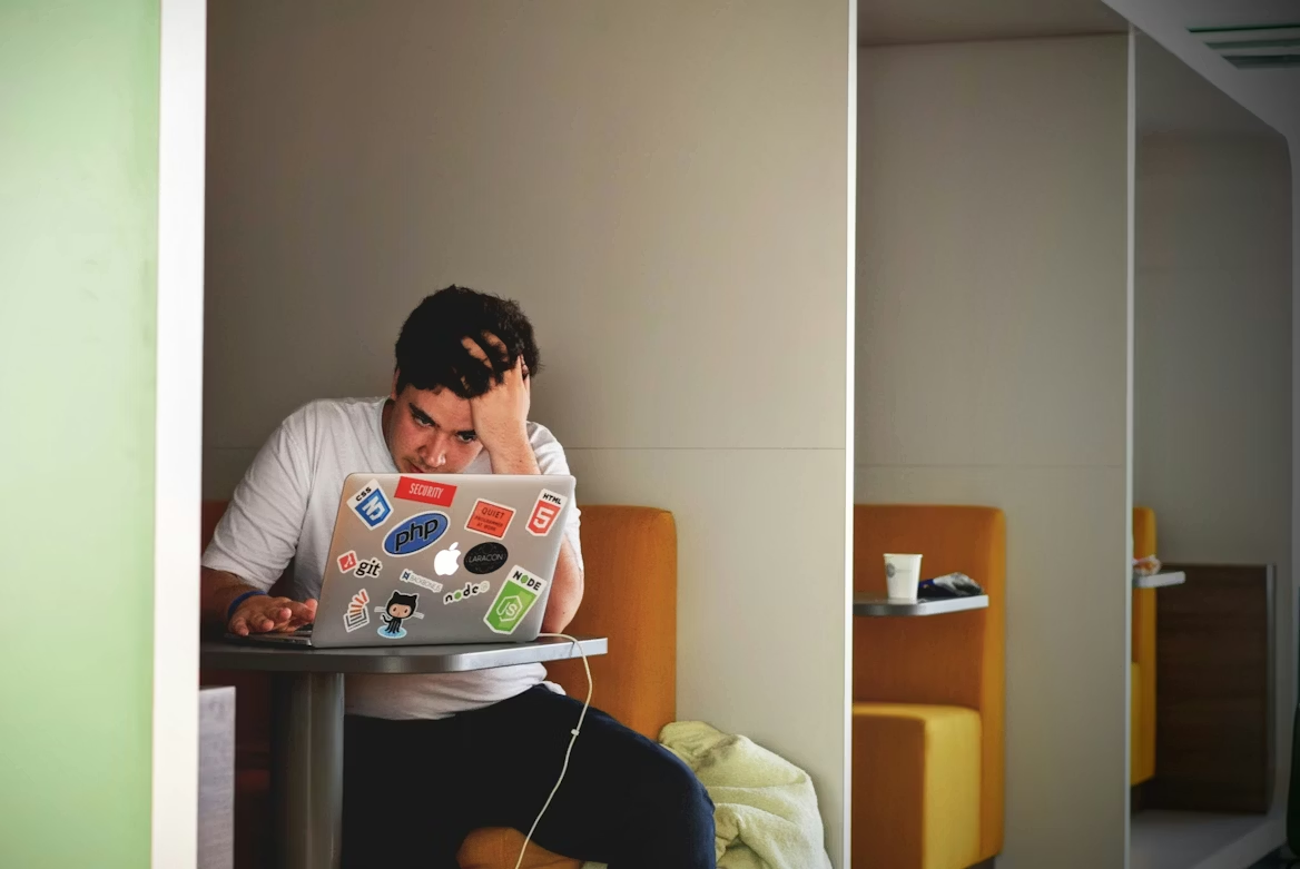 A frustrated man in a booth looking at his laptop screen